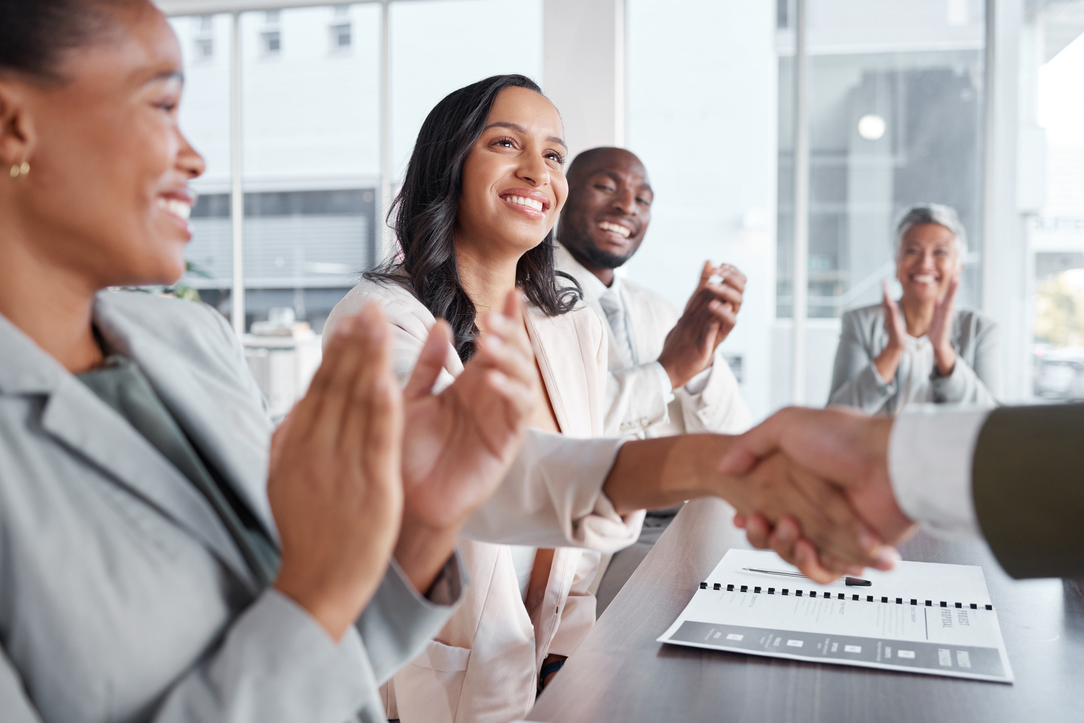 Woman shaking hands with someone while those around her applaud.