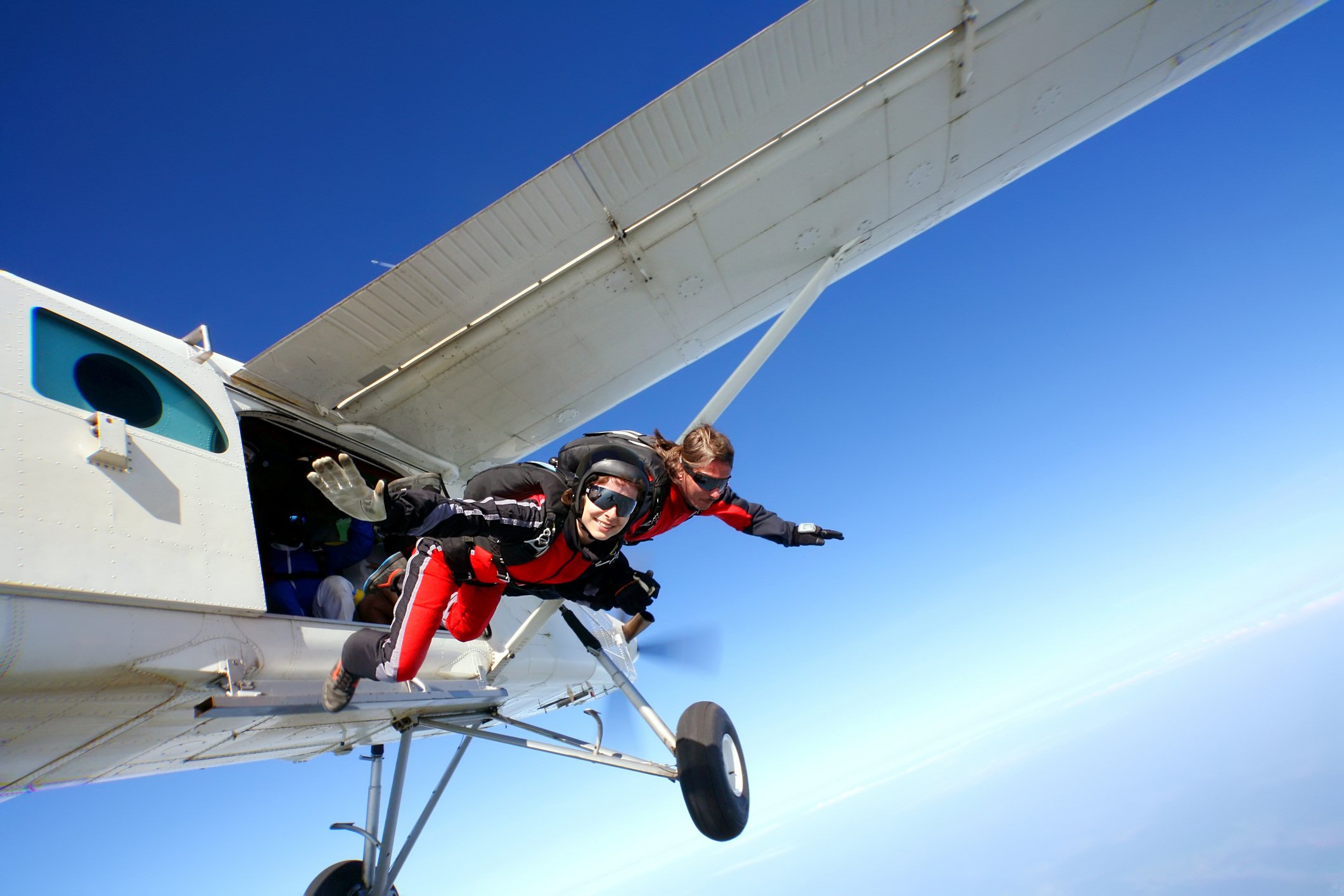 Two people in red jump suits jump tandem from an airplane together.